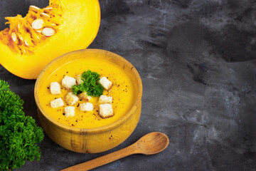 Pumpkin soup with cream, bread and fresh parsley in a rustic metal plate over grunge black background. Top view, copy space