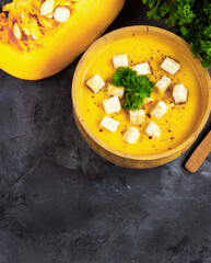 Pumpkin soup with cream, bread and fresh parsley in a rustic metal plate over grunge black background. Top view, copy space