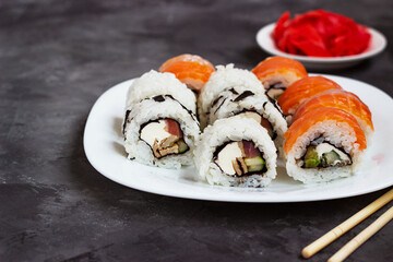 sushi rolls on a white plate on a black background with pickled ginger