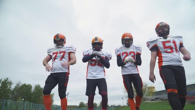American football training day, athletic football players in protective gear walk along the playing field.