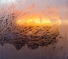 The light of the setting sun through the frosty pattern on the glass in winter