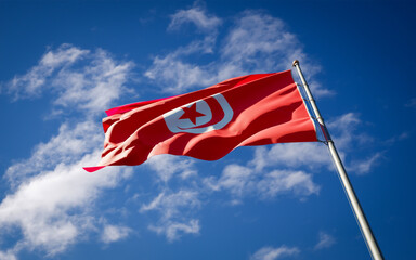 Beautiful national state flag of Tunisia fluttering at sky background. Low angle close-up Tunisia flag 3D artwork.