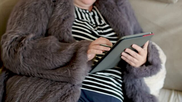Frau in einer Kaninchenfell Jacke arbeitet mit einem Tablet PC im Homeoffice  