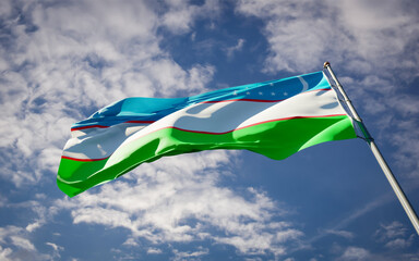 Beautiful national state flag of Uzbekistan fluttering at sky background. Low angle close-up Uzbekistan flag 3D artwork.