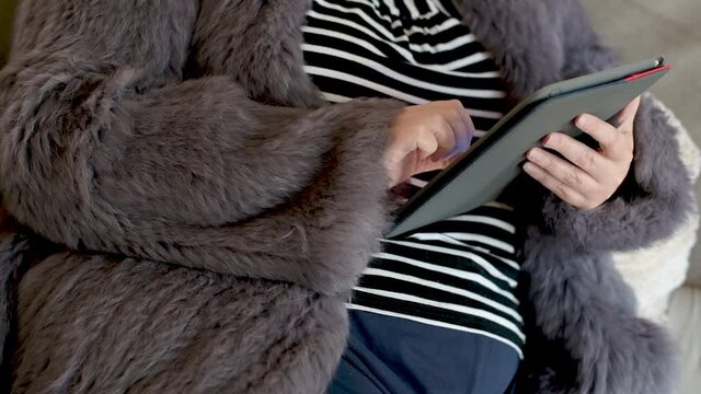 Frau in einer Kaninchenfell Jacke arbeitet mit einem Tablet PC im Homeoffice  
