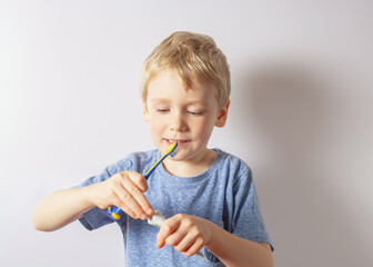 a boy with white hair holds a brush in his hands and squeezes the paste out of the tube onto the brush. Gray background.