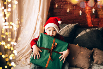 A boy holding a large box in a green package and a bow with a gift. Christmas mood
