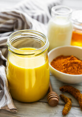 Yellow turmeric latte drink. Golden milk with cinnamon, turmeric, ginger  and honey over white wooden background.
