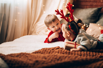 Brother and sister play with each other on a large bed. Christmas mood. Gift wrapped in paper and bowknot