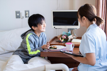 女性看護師の付き添いで自分で食事を食べる入院中の男の子