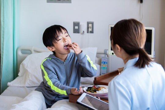 女性看護師の付き添いで自分で食事を食べる入院中の男の子