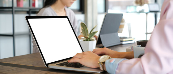 Cropped shot of two female colleagues working on computer tablet with white screen in meeting room.