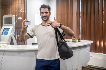 Bearded male standing at recepion desk, holding club card, pointing at it