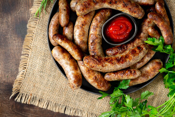 Fried sausages. Bavarian and Nuremberg sausages with spices and sauce. Delicious meat sausages in a black ceramic plate on a brown wooden table. German dish
