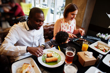 Happy multiethnic family with boy kid spend time at restaurant. Relationships of african man and white european woman.