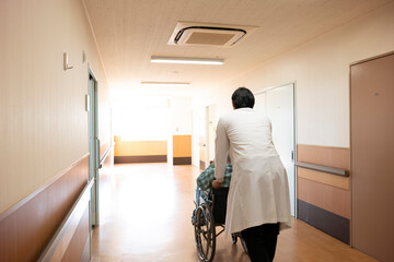 車椅子を押して進む医師と高齢男性の患者