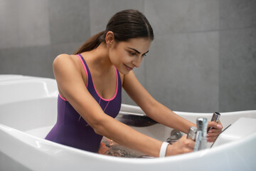 Dark-haired female sitting in hydromassage bathtub, receiving hydrotherapy