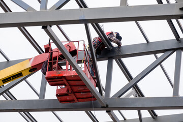 Man worker on a crane performs high-rise work on welding metal structures of new tower at height.