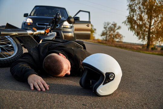 A motorcyclist lies on the asphalt near a motorcycle and car.