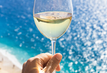 A glass of white wine in a man's hand. Wine against the backdrop of the sea coast and a sunny summer beach. Wine tasting and relaxation at the resort