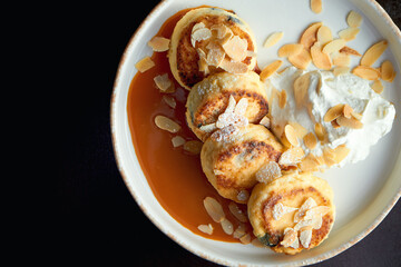 An ideal breakfast - Cottage cheese pancakes with caramel, almonds and cream sauce in a white plate. Ukrainian syrniki