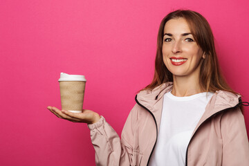 Smiling young woman in jacket holding paper roll on palm on pink background.