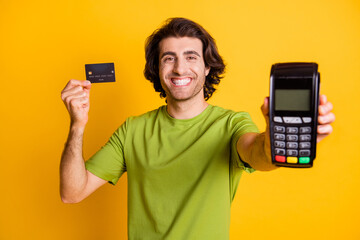 Portrait photo of smiling cheerful man keeping bank credit card smiling showing blurred terminal isolated on vivid yellow color background