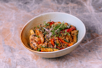 warm salad with shrimp, zucchini, tomatoes, pepper and mixed greens in blue clay bowl over marble background. Healthy food, clean eating, dieting, top view