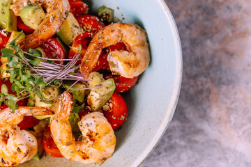 salad with shrimp, avocado, tomatoes and mixed greens in blue clay bowl over marble background. Healthy food, clean eating, dieting, top view, close up photo.