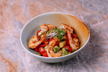 salad with shrimp, avocado, tomatoes and mixed greens in blue clay bowls over marble background. Healthy food, clean eating, dieting, top view