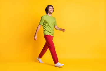 Fototapeta na wymiar Full length body size photo of man hurrying up stepping forward smiling in red trousers isolated on vibrant yellow color background