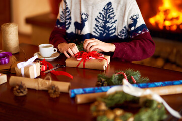  Men's hands hold Christmas present. Man using red ribbon, green fir tree twig to create Christmas gift. Wintar holiday. 