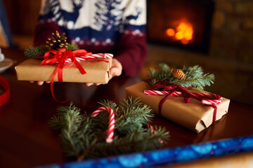  Men's hands hold Christmas present.  Man using red ribbon, green fir tree twig to create Christmas gift. Wintar holiday. 