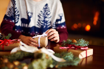  Men's hands hold Christmas present.  Man using red ribbon, green fir tree twig to create Christmas gift. Wintar holiday. 