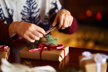  Men's hands hold Christmas present.  Man using red ribbon, green fir tree twig to create Christmas gift. Wintar holiday. 
