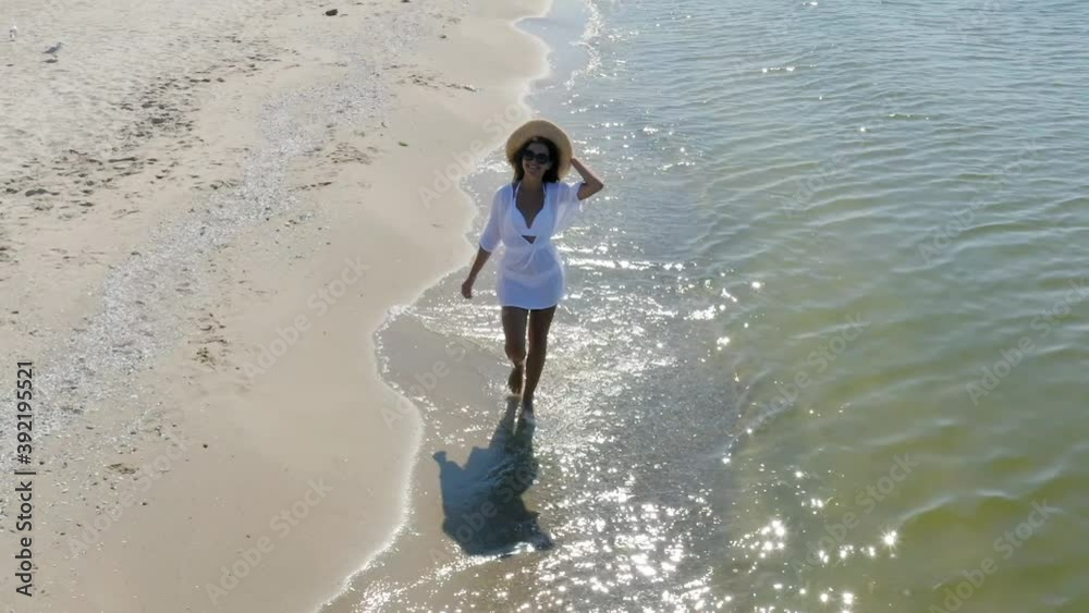 Wall mural Happy woman walking on sandy beach washed by sea waves, slow motion effect. Camera panning left