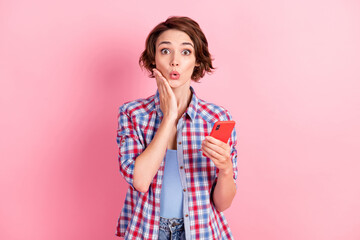 Photo of shocked adorable young woman wear checkered shirt holding modern gadget arm cheek isolated pink color background
