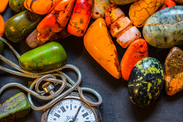 Old watch among colored pebbles.