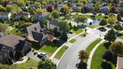 Overhead aerial view of colorful autumn trees, residential houses and yards with drainage pond along suburban street in Chicago area. Midwest USA. 4K
 - Powered by Adobe