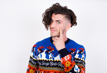 Young handsome Caucasian man wearing Christmas sweater against white wall, looking, observing, keeping an eye on an object in front, or watching out for something.