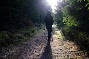 Active young person walking alone away in cold fresh sunny green forest road path way. Freedom...