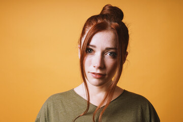 cool young woman with red hair messy bun hairstyle and loose strands at the front against yellow...