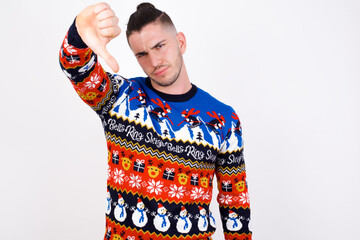Discontent Young handsome Caucasian man wearing Christmas sweater against white wall shows...