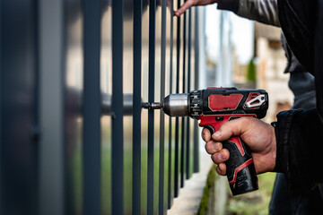 Metal fence installation. The worker is screwing the screw into the metal fence.