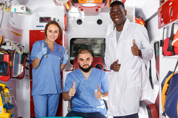 Portrait of three happy paramedicals posing in ambulance car outdoor