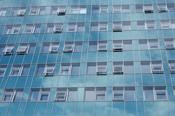 Fototapeta na wymiar A glazed modern office building in a business center that reflects the sky. Many closed and open windows.
