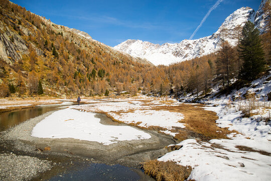 Man hiking distant in the Preda Rossa Valley scenery in late autumn, with the first snow on a sunny day. Val Masino, Lombardy, Italy.