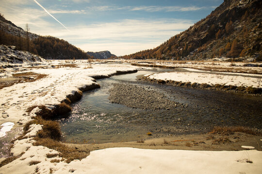 The river Duino flowing in the Preda Rossa Valley scenery in late autumn, with the first snow on a sunny day. Val Masino, Lombardy, Italy.