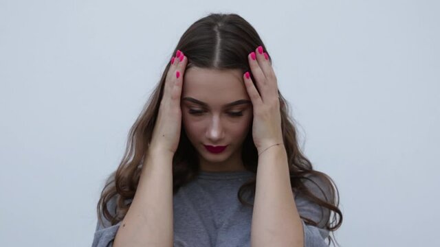  Beautiful worried brunette touches the face with her hands and bites her nails. Portrait of a nervous pretty girl on a gray background. frightened woman looks at the camera. FullHD footage
