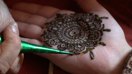 Close up macro shot of mehendi henna tattoo being applied in an intricate pattern on the hand of a...